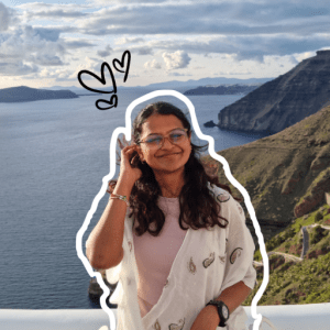 scenic view with a girl standing in front pushing back her hair with her right hand and smiling cheerfully at the camera